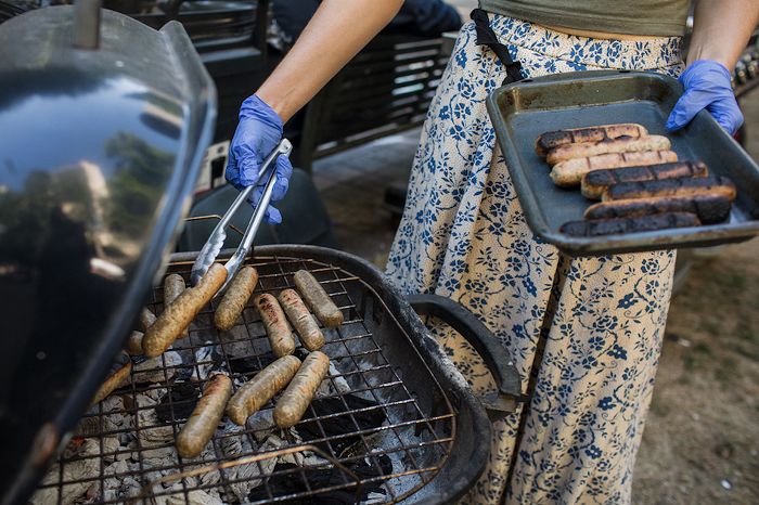 A volunteer grills vegan sausages, placing them on a tray.