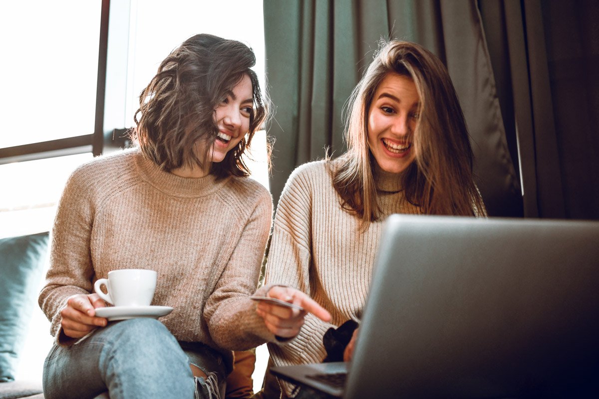 Two women smile and laugh as they look at their computer.