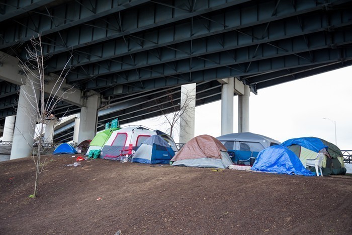 A cluster of tents under a highway overpass.