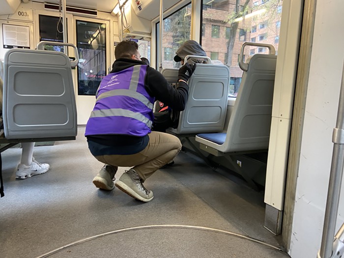 A person in a purple vest squatting next to a rider on the streetcar.