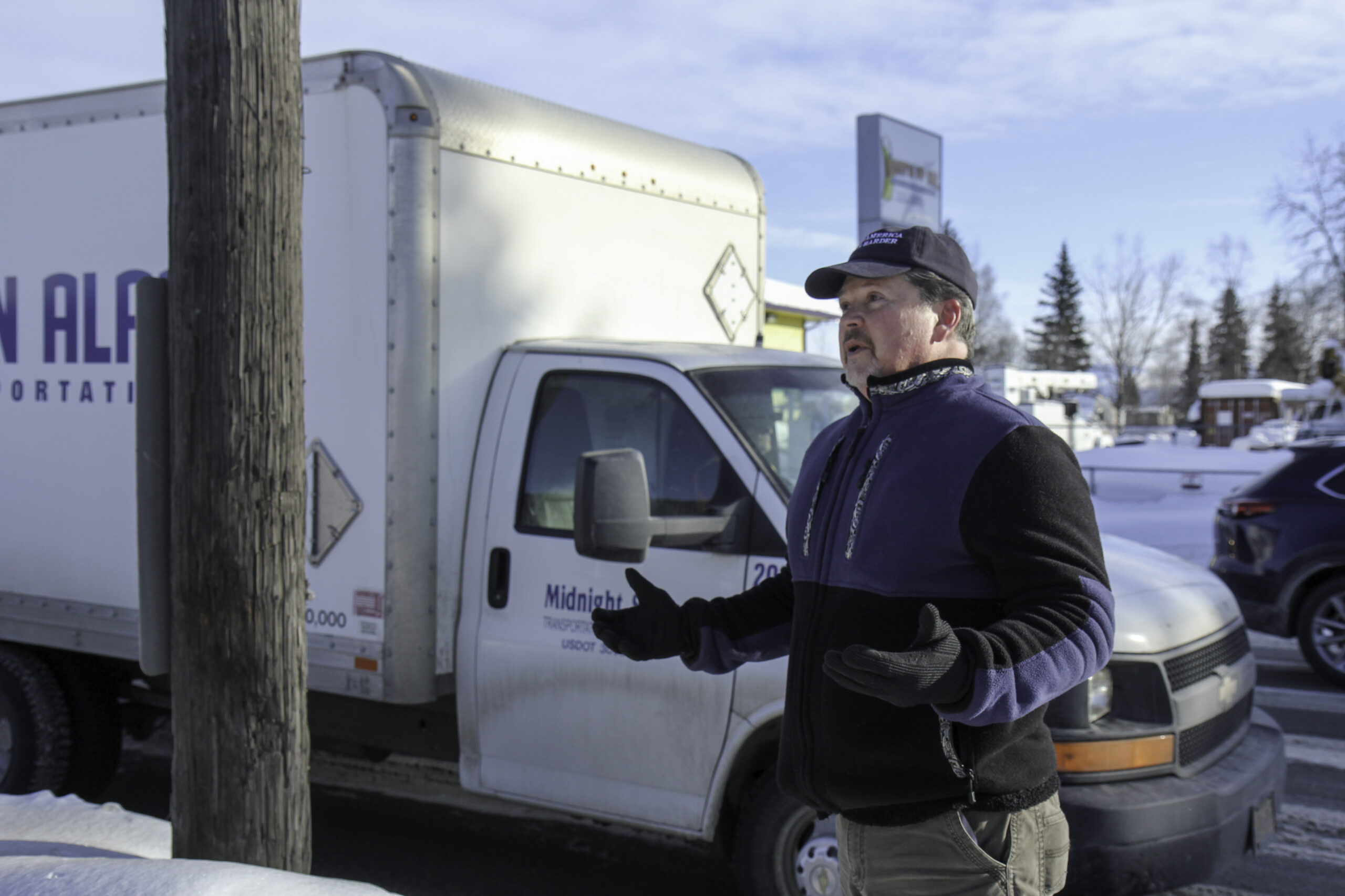 A man with a hat is standing on a sidewalk next to a utility pole.